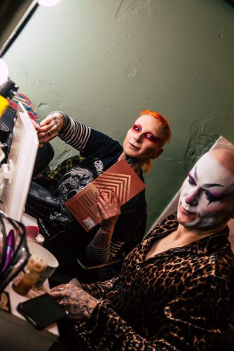 burlesque_025 Zwei Burlesque-Performerinnen sitzen backstage vor dem Spiegel, umgeben von Make-up und Requisiten, während sie sich auf ihren Auftritt vorbereiten.
