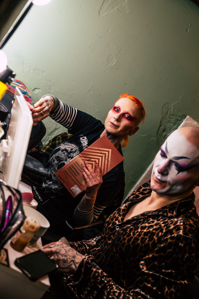 burlesque_025 Zwei Burlesque-Performerinnen sitzen backstage vor dem Spiegel, umgeben von Make-up und Requisiten, während sie sich auf ihren Auftritt vorbereiten.