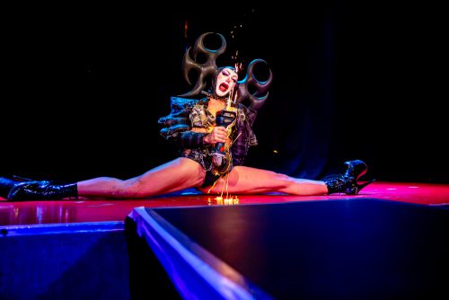 burlesque_06 Harpy Fatale sitzt im Spagat auf der Bühne und performt mit einer Schleifmaschine, Funken sprühen über den Boden.