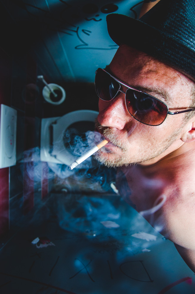 Künstlerportrait von Oliver Rieche mit Sonnenbrille und Zigarette in atmosphärischem Licht, aufgenommen für eine Sedcard.